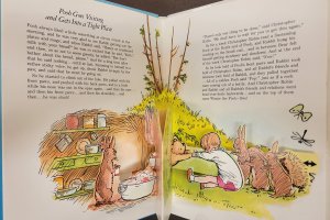An open pop-up book that says, "Pooh Goes Visiting and Gets into a Tight Space" and an illustration with Pooh stuck in a hole with Christopher Robin trying to pull him out. Winnie-the-Pooh: A Pop-up Book, by A. A. Milne et al., 1st ed., E.P. Dutton, 1984.