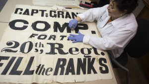A conservator works on the restoration of a Civil War banner that says "Fill the Ranks"