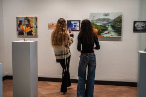 Seen from behind, two visitors view student work hanging on the wall at the 2025 SEC exhibition.