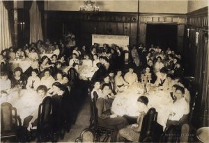 A sepia toned image of girls in the Martha Cook Dining Hall seated for a meal. Every table is full.