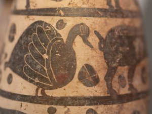Close-up of a small buff-colored Italo-Corinthian alabastron painted with a bird following a pig.