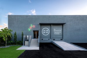 The exterior of El Espacio 23, a grey concrete warehouse featuring a large white "23" logo on its roll-up doors.
