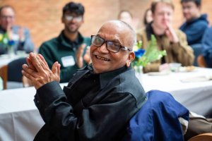 Murty smiles and claps while sitting at the IOE Grad Banquet