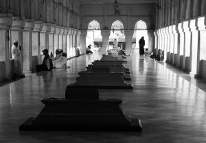 Black-and-white photo of people sitting and standing in a long, sunlit colonnaded hall, with a row of raised stone tombs extending down the center.