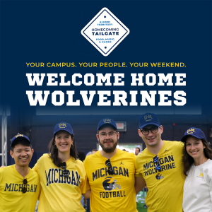 A group of smiling people in Michigan Wolverine shirts and hats pose together under a welcome banner.