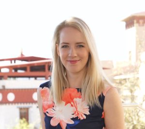 A blonde woman in a navy dress with coral-colored flowers on it smiles for the camera