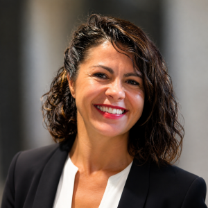A brunette woman in a white shirt and black blazer smiles for the camera