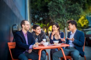 Four people at a table outdoors drinking coffee and laughing