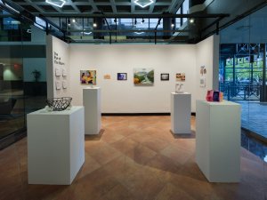 Student work - including 2d pieces hung on white gallery walls, and 3d objects displayed on pedestals - is installed in a gallery space for Eye of the Storm, the SEC's Fall 2025 exhibition.