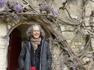 Dr. Virginia Krause smiles at the camera while standing beside a stone archway covered in twisting wisteria vines with purple blossoms.
