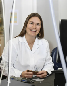 A woman in a white shirt smiles at the camera from behind a desk