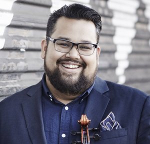 Headshot of Vijay Gupta with a beard and glasses showing the top of his violin.