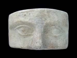 Rectangular piece of gray-white clay shallowly carved with two eyes and a nose.