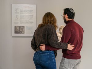 A man and a woman, with an arm around each other, pause to read a panel and view a marble statue in the Kelsey Museum.