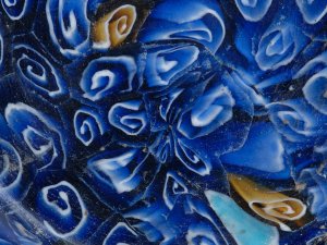 Close-up of a vibrantly colored millefiori glass dish, showing white swirls over a blue background, shot through with occasional sections of turquoise and gold.