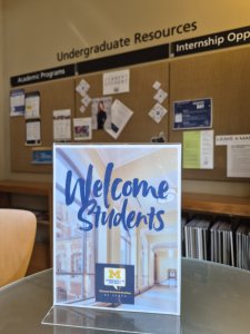 A sign reads: Welcome Students. Behind it is a posting board with student resources.