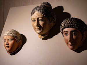 Three Egyptian mummy masks: a man with straight hair and a goatee, a woman with her hair in a bun, and a curly-haired man with a mustache.