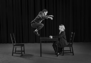 Man jumping onto table while woman sits on the other side