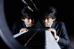 Man staring down piano keyboard with the keys and his face reflected in the piano