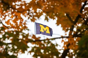 The Michigan Union flag is framed by orange leaves on a nearby tree on a fall day.