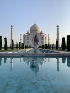 A young woman standing in front of the Taj Mahal with a pink scarf wraped around her shoulders and head