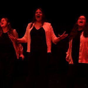 Three actors illuminated by dim, red light.