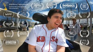 Young man in a Red Sox jersey smiles, sitting in wheelchair, in an outdoor location. The names of 19 film accolades show around the main character in the image.