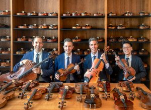 Four men holding string instruments in a studio with many violins