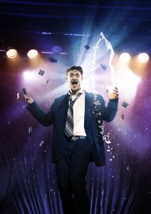 Mann holding microphone with various items flying in the air around him