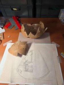 Ceramic sherds reassembled into two sections on a table next to a line drawing of a vessel