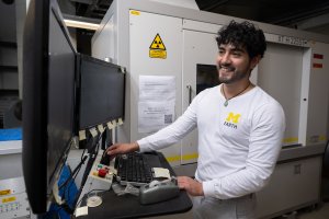 A man smiles at a computer monitor in front of a CT scanner