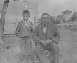 A young boy stands next to an Odawa elder man who is seated.