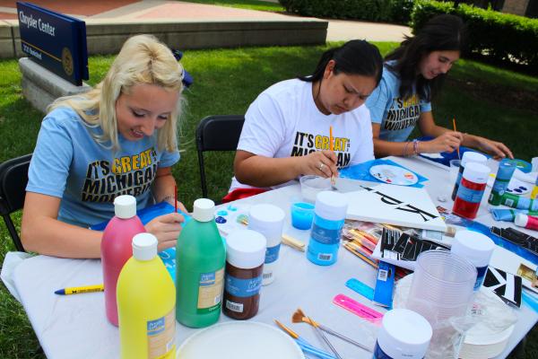 Two women painting on canvases at a table outdoors