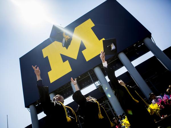 students throwing up their graduation caps in front of the football stadium