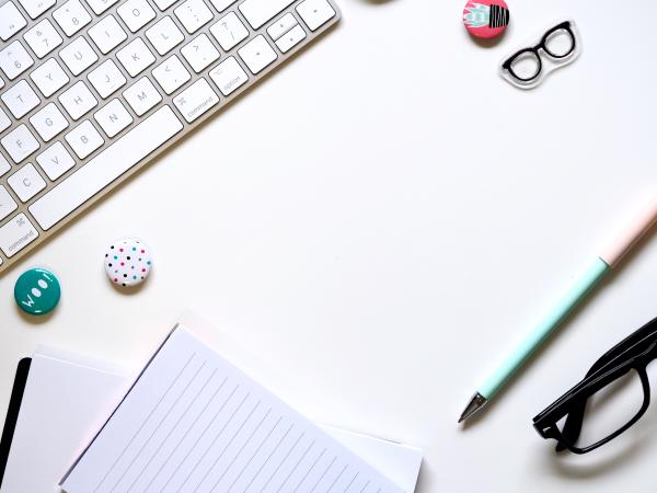 colorful pens, glasses, notepads, buttons, and a keyboard on a desk