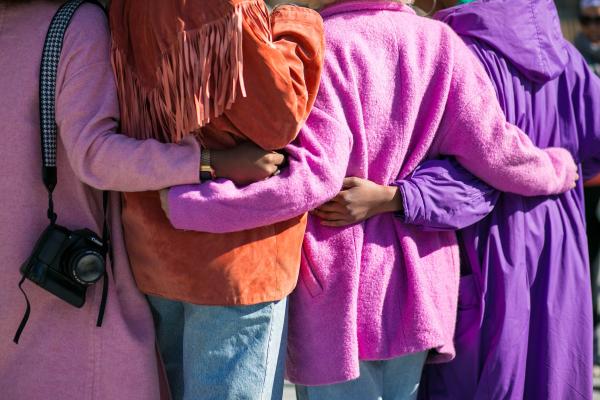 Four individuals, with arms around each other wearing pink, orange, and purple.