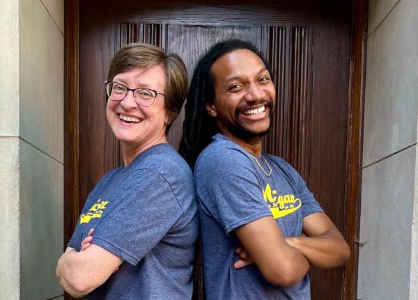 The directors of MCSP--a middle aged white woman and a younger Black man--standing back-to-back with their arms crossed, smiling at the camera