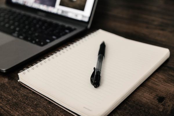 an open laptop that's next to a notepad, with a pen on top of the notepad