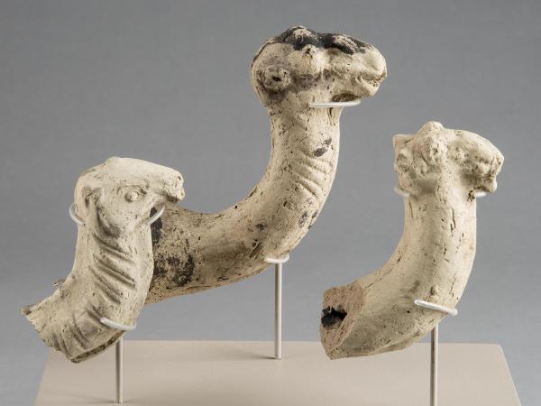 Broken-off heads and necks of three whitish stone camel figures. The fragments are suspended in the air using a series of mounts.