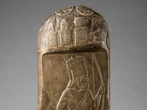 Plaster cast of a kudurru with a rounded top. The document shows a bearded king wearing a crown and carrying a bow.