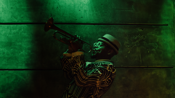 Etienne Charles playing trumpet in a very green room.