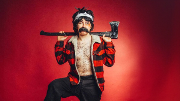 Natalie Palamides in drag holding an axe in front of a red background.