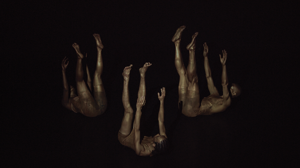 Three dancers from TRIBE, seemingly falling surrounded by darkness with their arms and legs extended into the air.