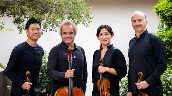 Four members of Takács stand in a line with their instruments smiling.