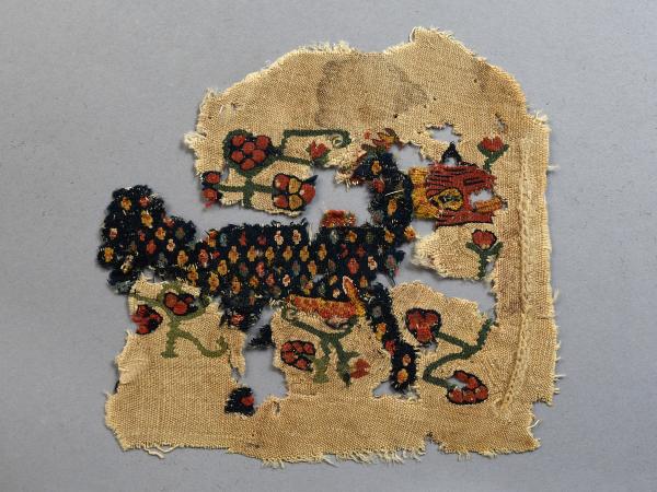Textile fragment depicting a polka-dotted warhorse surrounded by floral and vine motif.