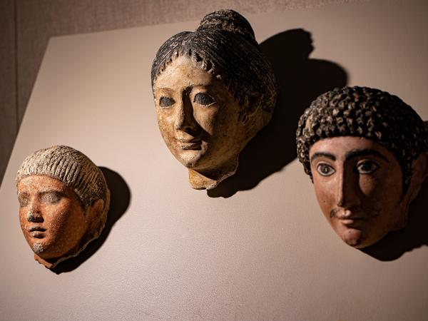 Three Egyptian mummy masks: a man with straight hair and a goatee, a woman with her hair in a bun, and a curly-haired man with a mustache.