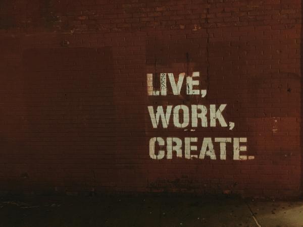 "live, work, create" painted in white block letters on a dark red wall.