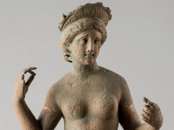 Head and shoulders of a nude statue of the goddess Aphrodite, standing with her arms upraised and wearing a diadem.