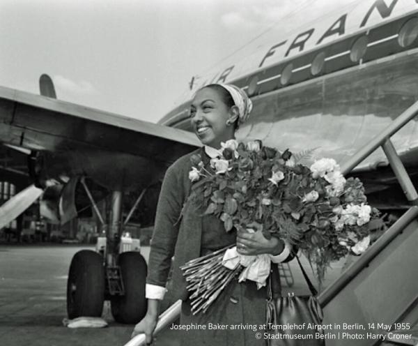 Young woman, in 1955 Berlin, stands in front of air france airplane holding a large flower bouquet.