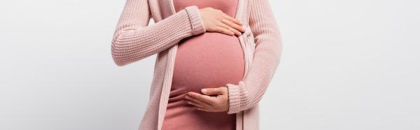 A pregnant person is wearing a dark pink shirt and a light pink sweater and holding their stomach
